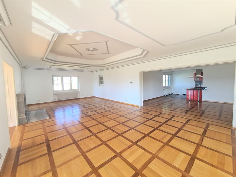 Spacious living room with hardwood flooring in a geometric pattern, white walls, and a decorative ceiling with recessed lighting.