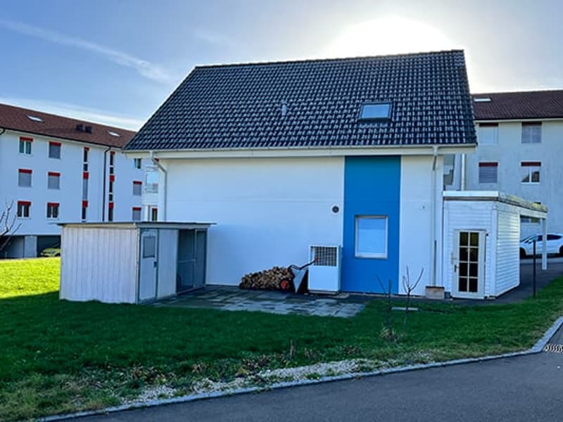2-story house with a blue door, white exterior walls, and a black tiled roof. There is a garage and a parking space visible on the property.