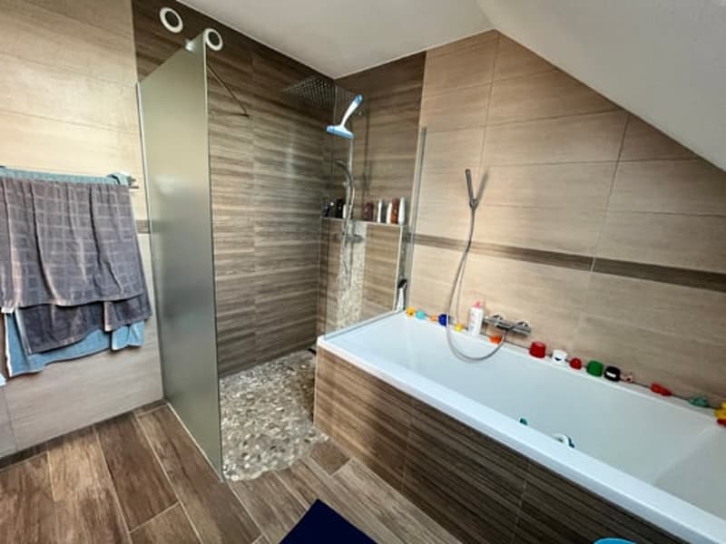 Large bathroom with a bathtub, glass-enclosed shower, wooden-style tile walls, and shelving for toiletries