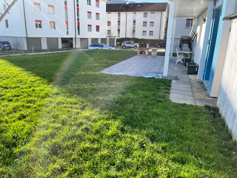 Multi-story apartment building with a grassy courtyard and parking spaces in the foreground.