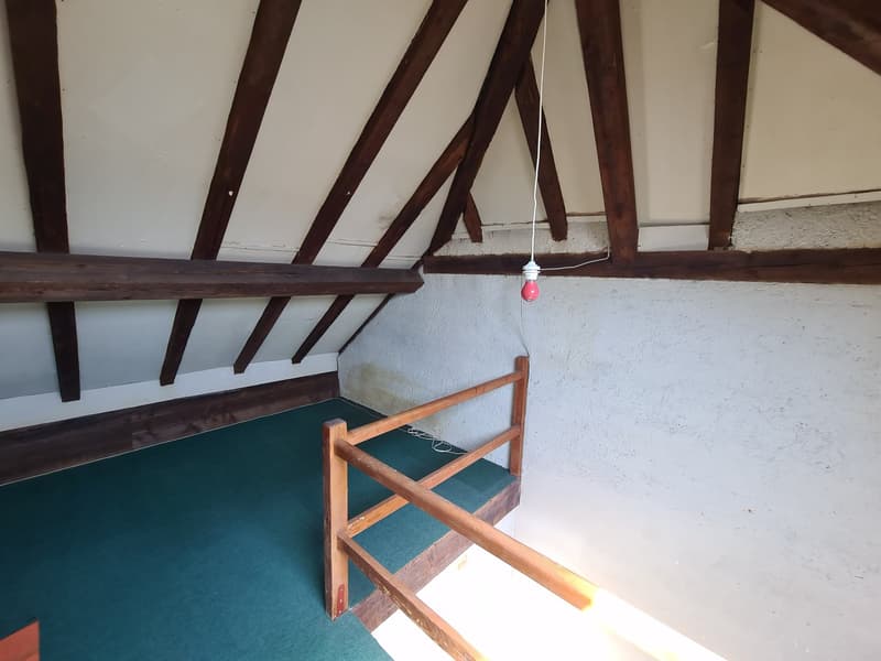 Attic space with exposed wooden beams, green carpeted floor, and a wooden chair