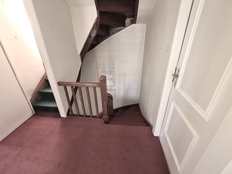 Wooden staircase with railing, leading to a room or floor above. The stairs are carpeted in a dark color.