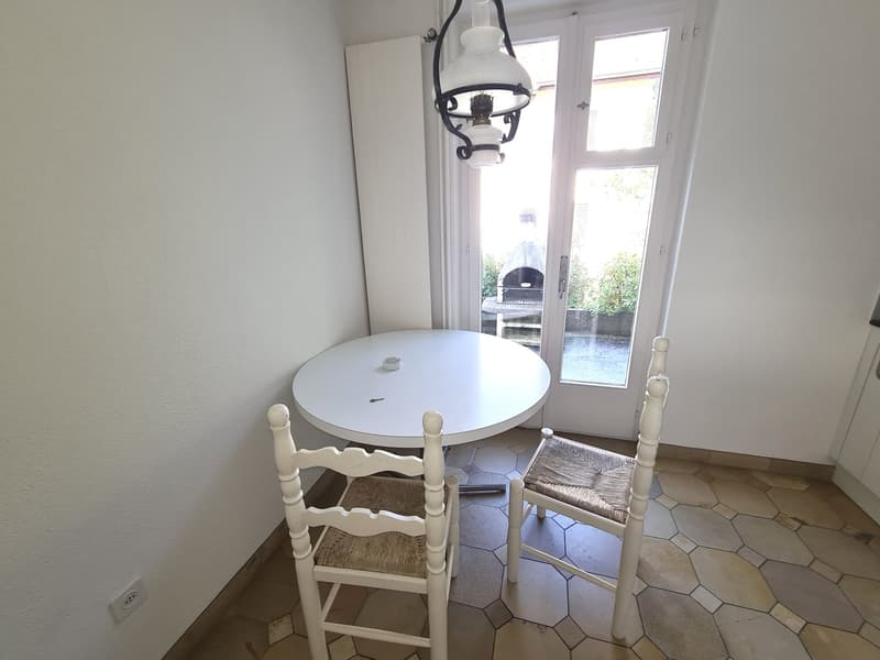 White round dining table with wooden chairs, hexagonal tile flooring, large window with view of outdoor patio area