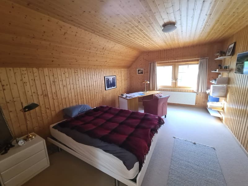wooden walls, bed with blanket, bedside cabinet, desk with lamp, chair, carpet