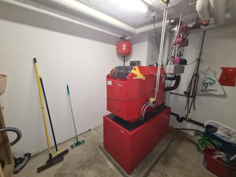 Heating equipment, pipes, buckets, storage box, a red and white bag, two brooms, one with a green handle
