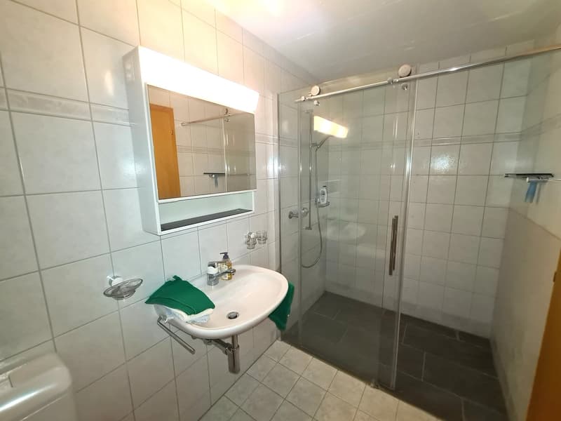 bathroom with shower, sink, toilet, mirror, green towels, tiled walls and floor