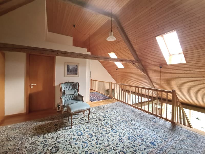 Wooden ceiling, carpeted floor, a chair, an ottoman, wooden stairs, picture frame, large windows