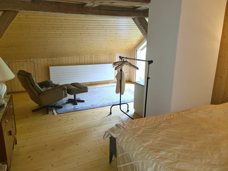 wooden floor, wooden walls, wooden bed, comfortable leather armchair, small ottoman, wooden dressing table, clothes rack, white radiator