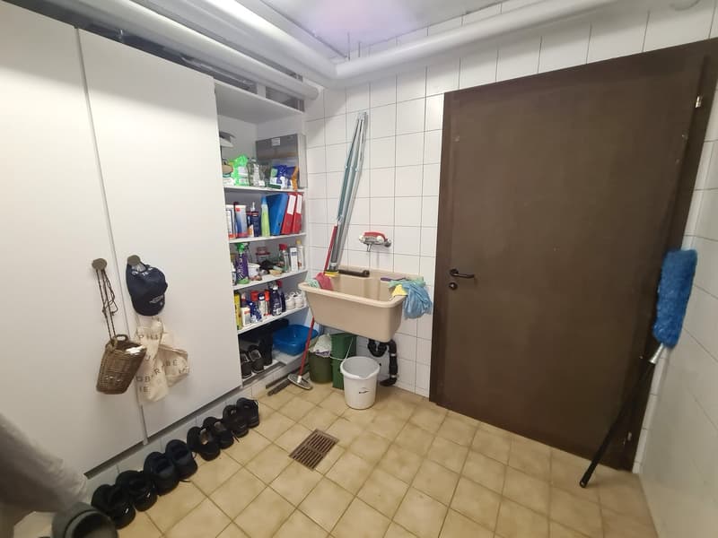A room with tile floor, washing machine, sink, white cabinet, storage boxes, cleaning tools, shoes