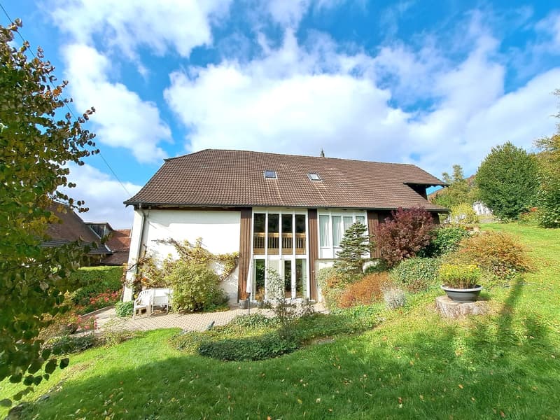 2 story house, brown roof, large windows, balcony, patio, white wall, green lawn, shrubs and plants