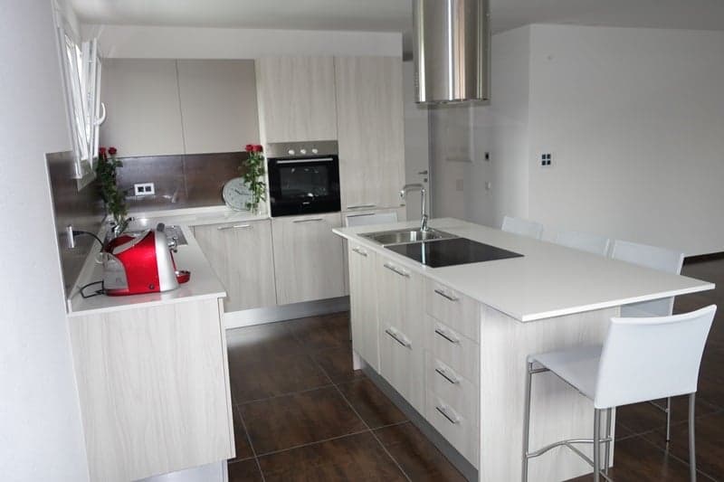 White cabinets, wooden floor, black stove, stainless steel oven hood, sink, bar stools