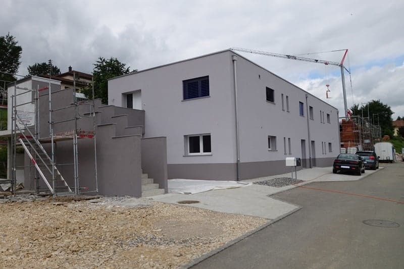 New building under construction, concrete facade, cranes on site, cars parked nearby