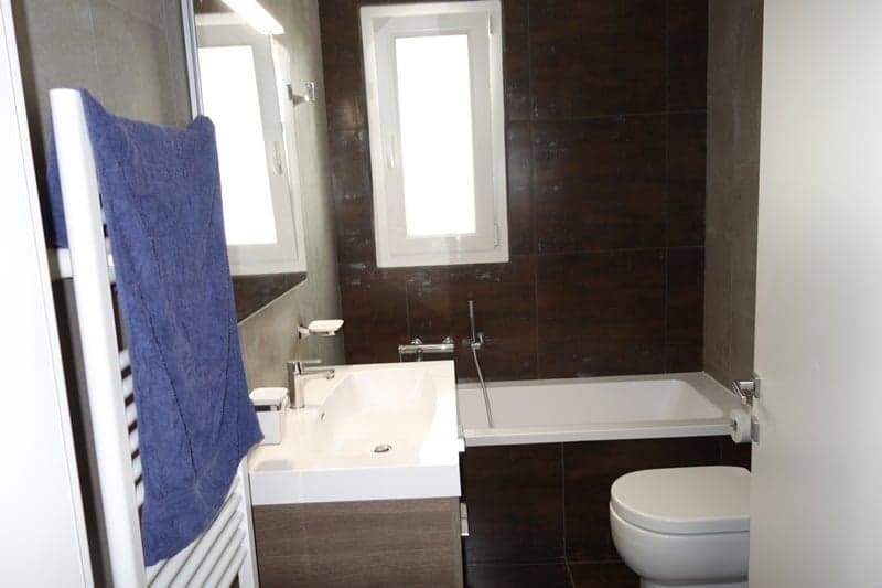 Bathroom: white sink, bathtub, toilet, blue towel, dark brown tiles, white toilet, white shower
