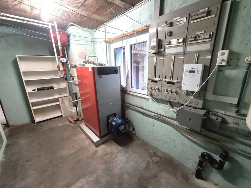 Room with gas heater, metal pipes, electrical panels, white shelves, cement floor