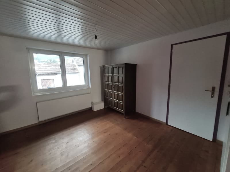 Empty room with wooden floor, white walls, a window, a radiator, and a cabinet.