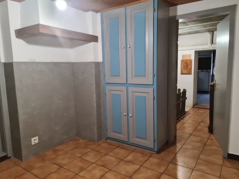 An empty room with a wooden plank on the wall, a blue and gray cabinet with two doors, and brown tile flooring.