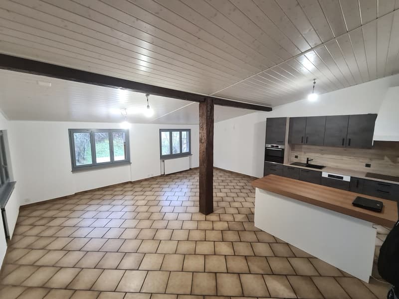 empty room with tiled floor, large windows, wooden beam, kitchen with oven and sink