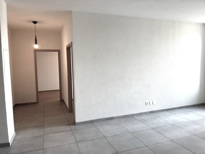 Empty room with tiled floor, white walls, two doorways, single light fixture