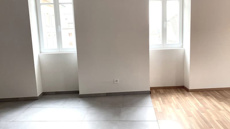 Empty room with windows on the left wall, gray floor, wooden floor on the right side