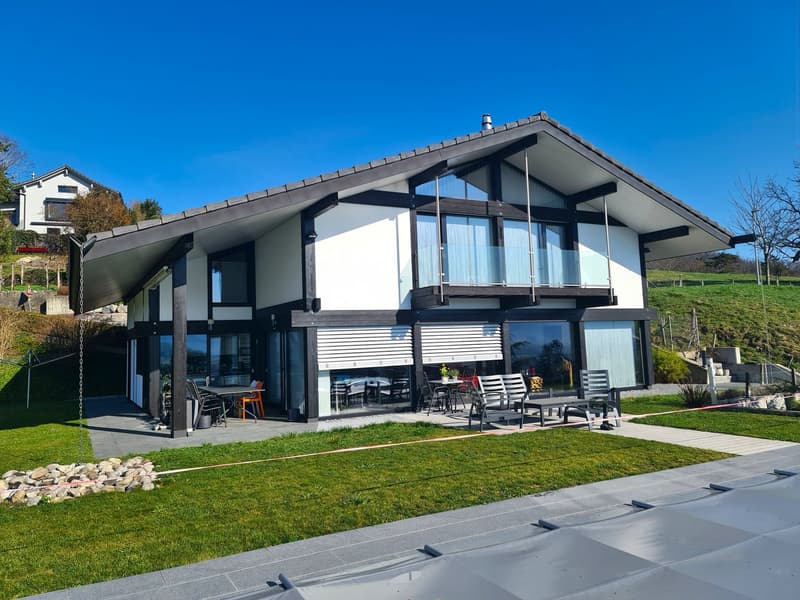 Modern house with white and black exterior, glass windows, glass doors, glass balcony, patio, garden, and outdoor seating area