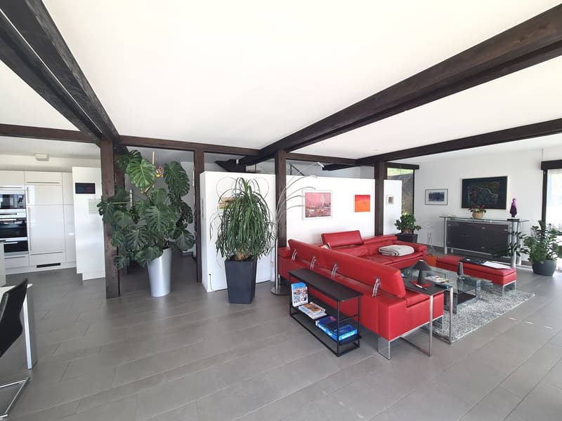gray floor, red couch, 2 large plants, 2 side tables, coffee table, artwork, ottomans