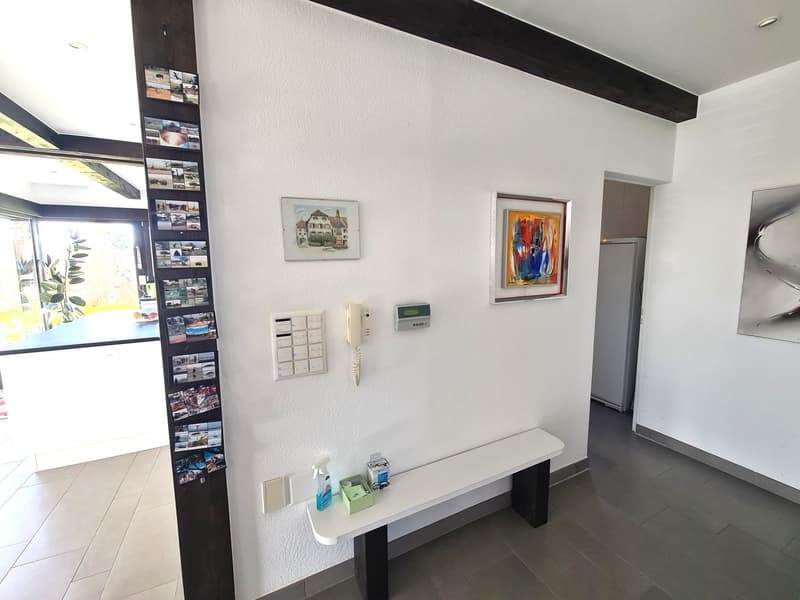 Modern minimalist design with white walls, gray flooring, small bench, mounted photo frames, wall-mounted telephone, and various items on the bench.