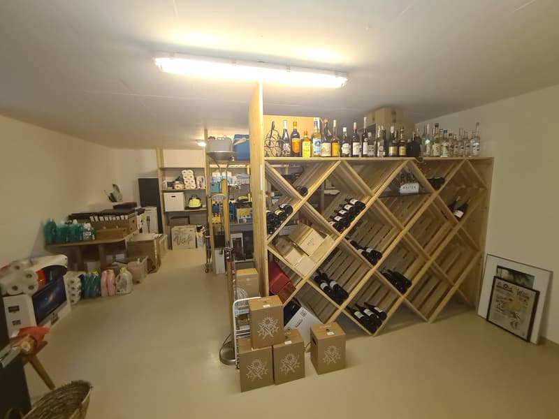 large wine rack with many bottles, bottles on shelves, boxes, framed picture, boxes, roll of toilet paper, basket, boxes with items on top