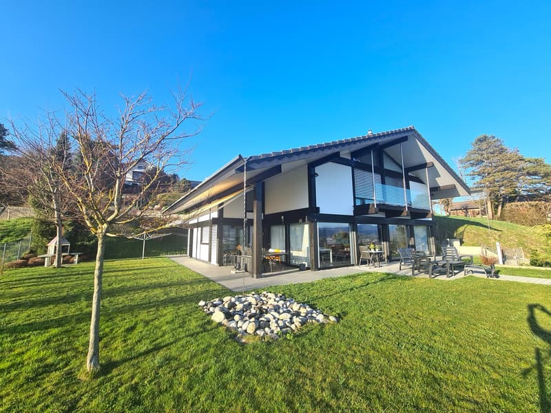 Modern house with glass walls, balcony, garden, terrace, patio with outdoor furniture, grassy lawn