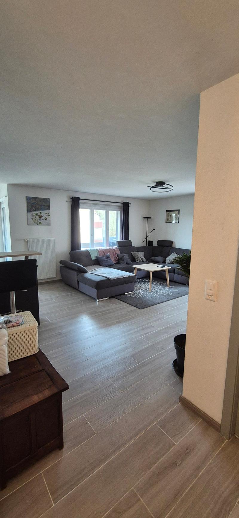 Living room: hardwood floors, L-shaped couch, coffee table, picture frames, floor lamp, potted plant, radiator