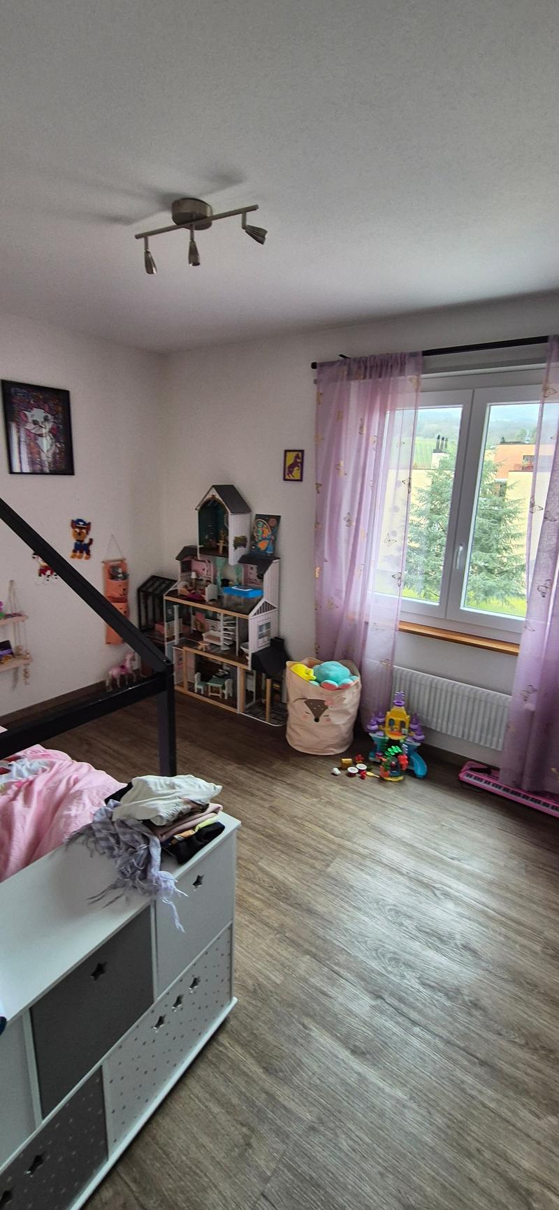 large window with purple curtains, toys on the floor, white shelf, wooden flooring, white walls