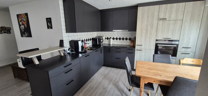 modern kitchen with black cabinetry, white tiled backsplash, wooden island, stainless steel appliances, and a dining area with wooden table and chairs