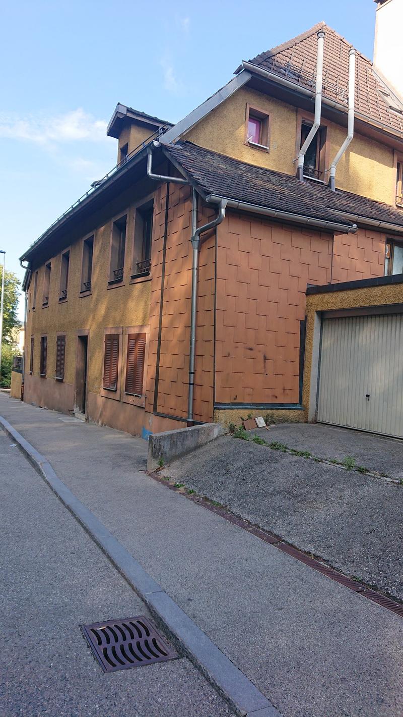 2-story building with yellow exterior walls, red tiled roof, and a garage door on the ground floor. The building has several windows and appears to be located on a residential street with a paved sidewalk.