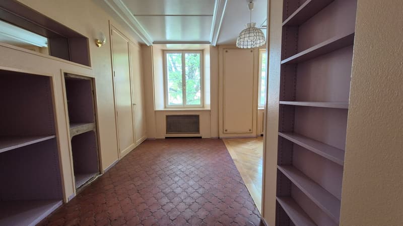 empty hallway with brown tile floor, wooden parquet floor, two sets of built-in wardrobes on each side, two small windows, a heater below the window, and a lamp hanging from the ceiling