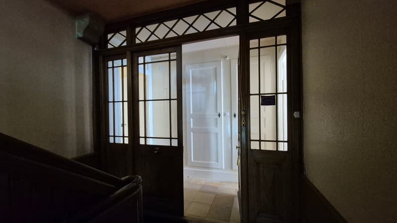 Large wooden doors with glass panels, staircase on the left, tiled floor