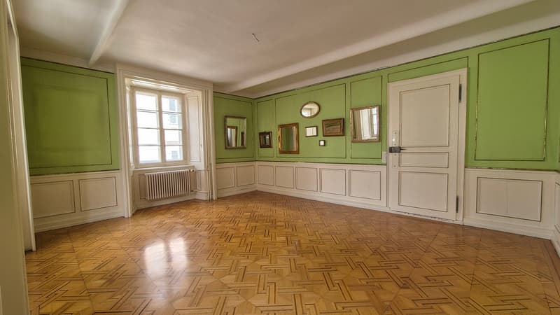 Green walls, wooden floor, white door, several mirrors, white radiator, white windows