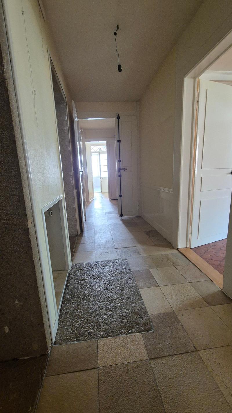tiled floor, white walls, doorways on both sides, small rug in front of one door, black bars on the door, open doorway in the distance, wire hanging from the ceiling