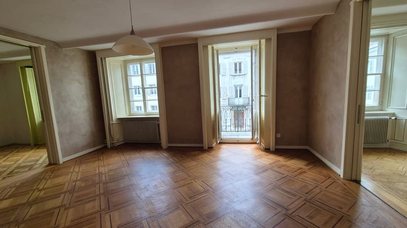 Parquet floor, arched doorways, large windows, radiators, balcony with a railing, and a ceiling lamp.