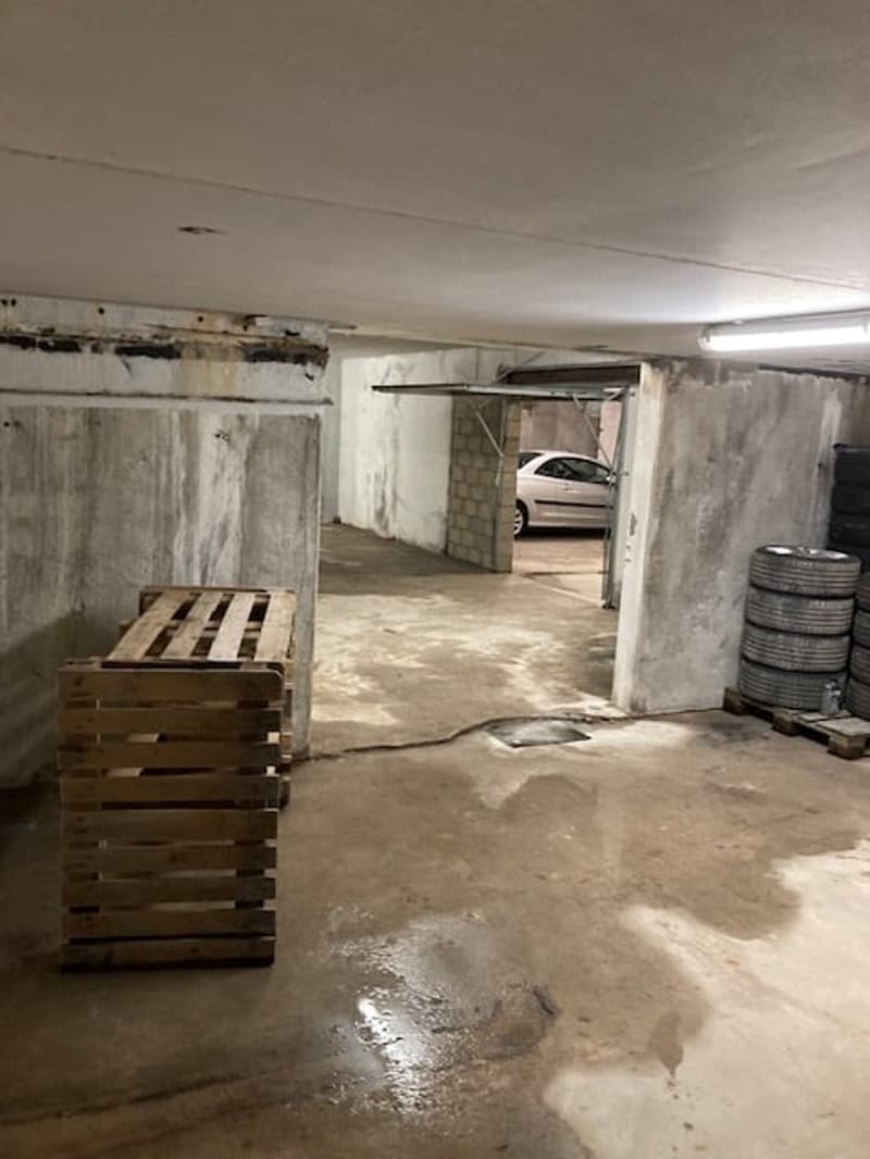 concrete floor, grey walls, car parking, wooden storage pallet, light fixture on ceiling, stack of tires