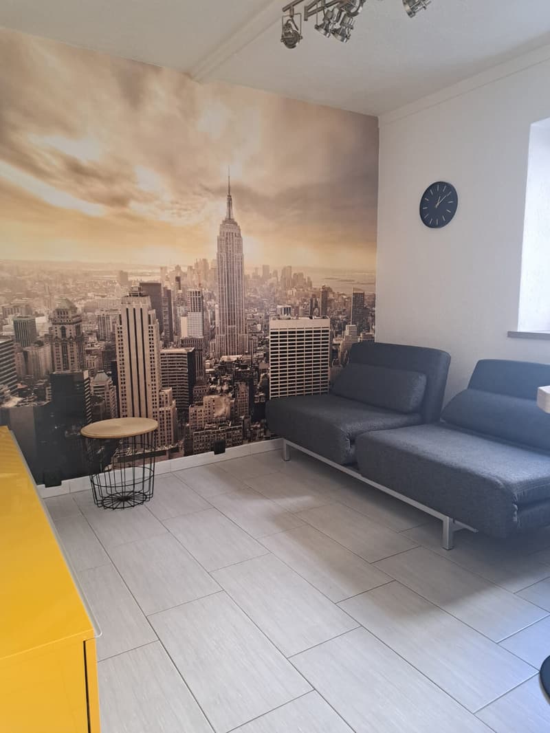 Living room with sofa, side table, large wallpaper mural, tile floor