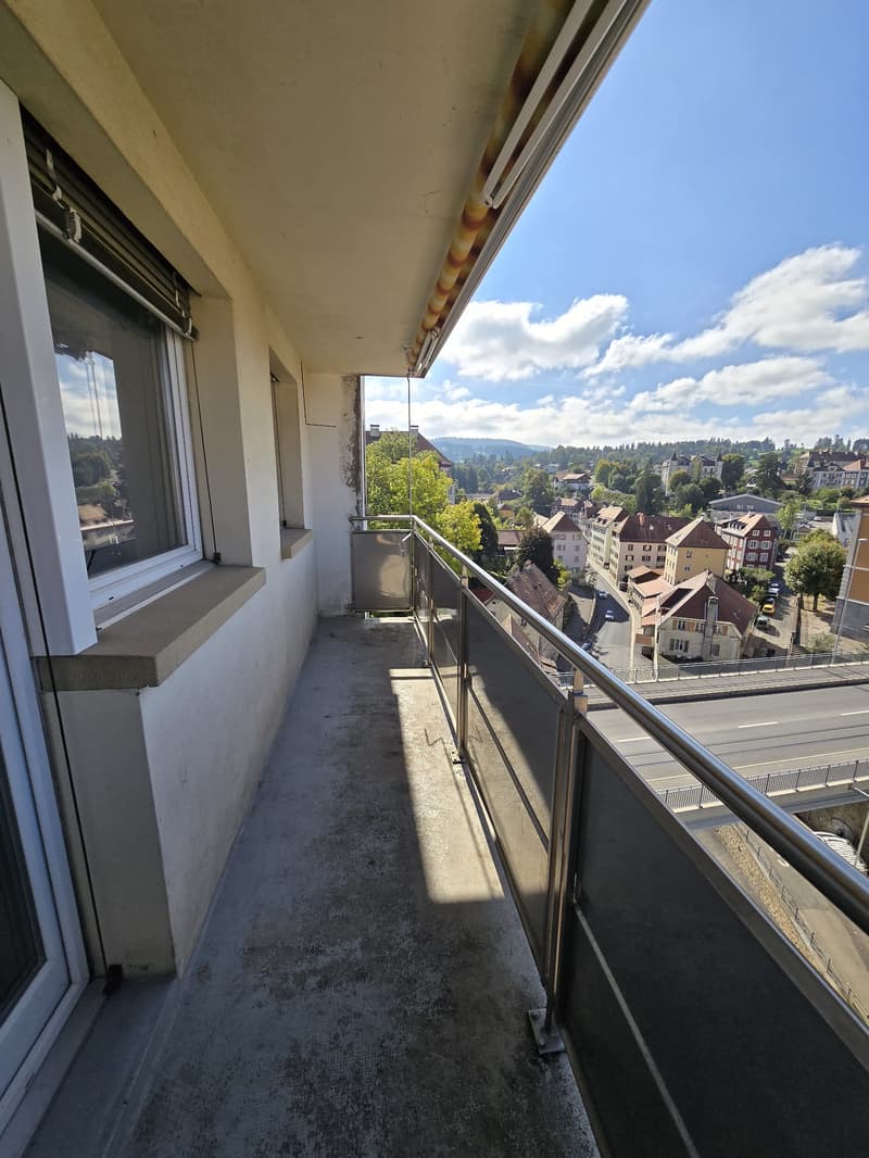 Balcony with metal railings, concrete flooring, overlooking cityscape and distant hills.