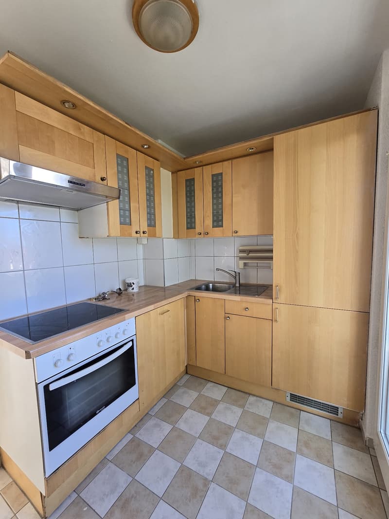 Open kitchen with white tiled flooring, wooden cabinets, integrated appliances including an oven and stove, under cabinet lighting, and tiled backsplash.