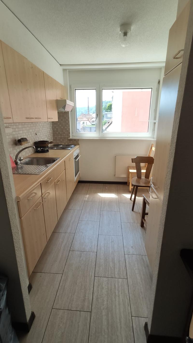 A kitchen with wooden cabinets, a tile floor, a stove and sink, and a window with a view