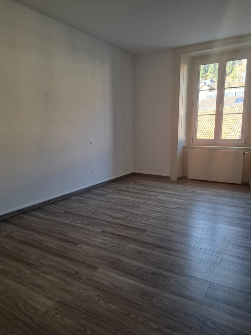 empty room, white walls, wooden floors, windows with view of outside, radiator