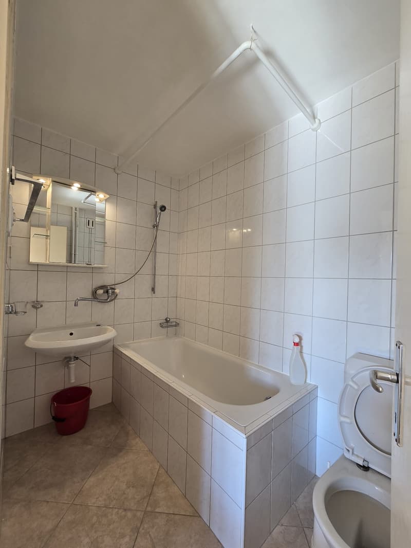 Bathroom: White bathtub, white tiled walls, white sink, mirror, showerhead, toilet