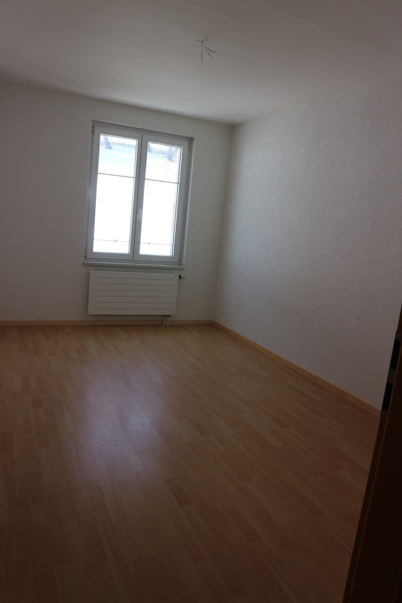 empty room with window, wooden floor and white walls, with radiator