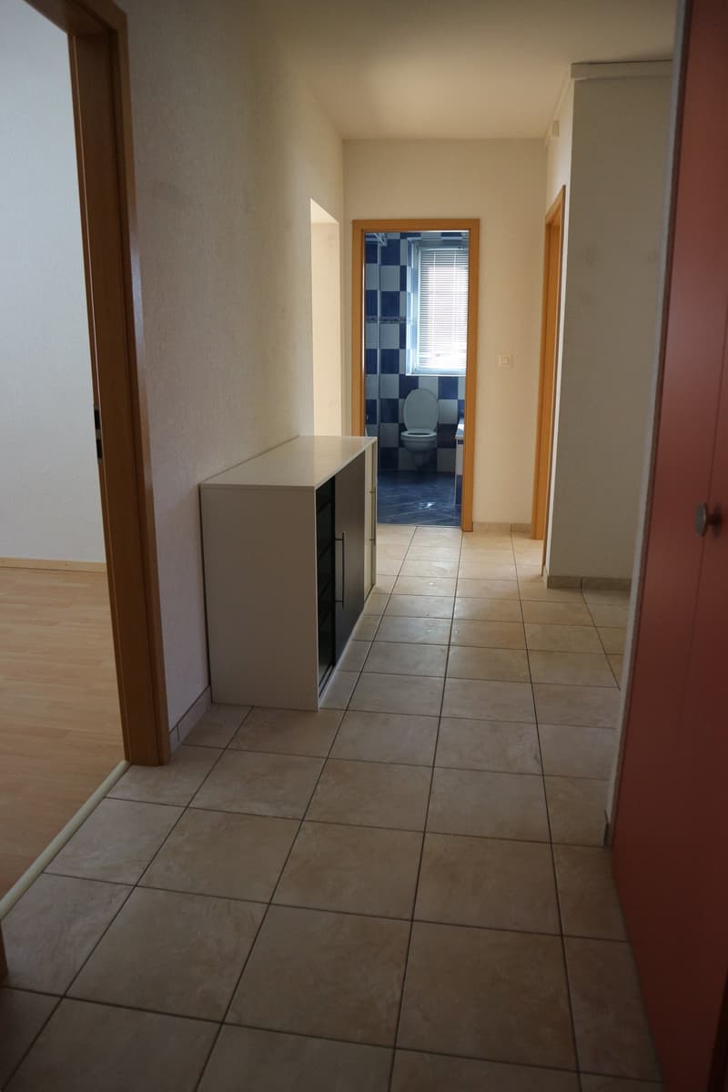 empty hallway, white tiles, small white cabinet, door to bathroom