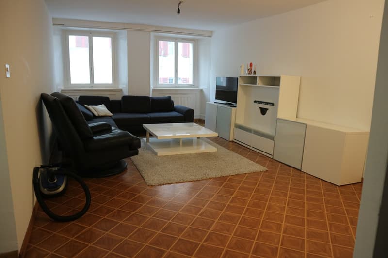 Living room: brown tile floor, white couch, coffee table, TV, beige rug, white entertainment center, white cabinets