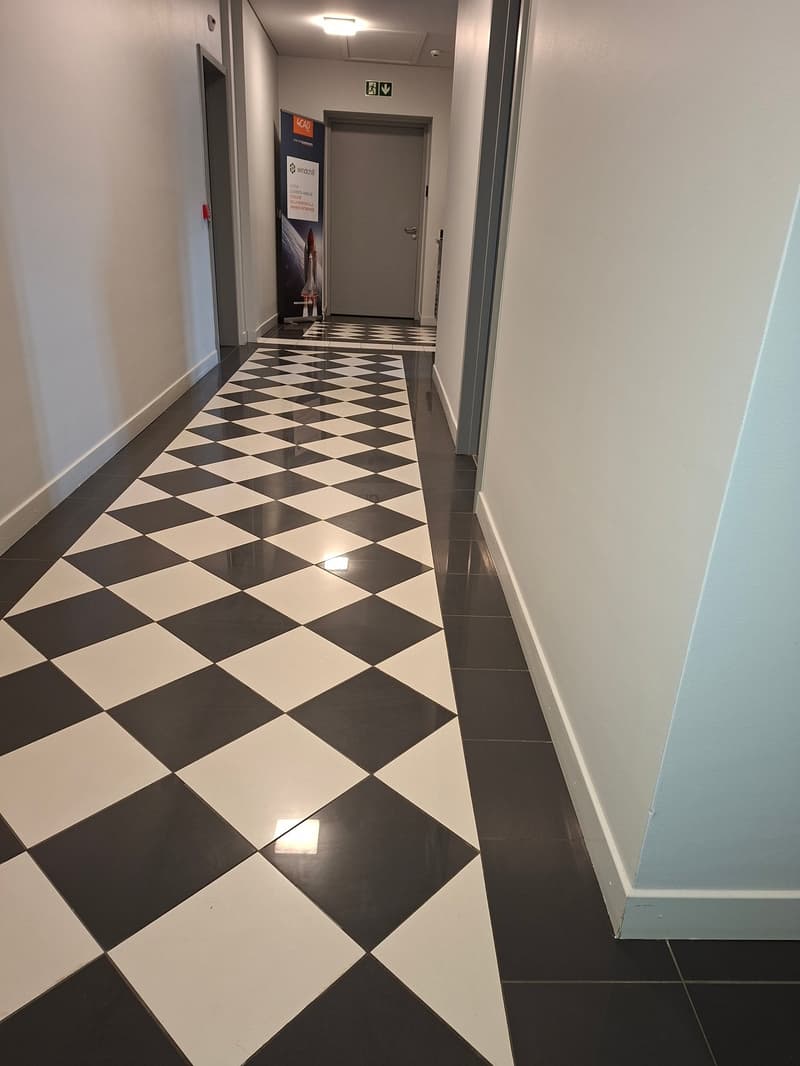 Black and white checkerboard flooring, white walls, grey door, sign with shuttle image