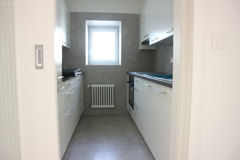 A modern kitchen with white cabinets, tiled flooring, stainless steel sink, and built-in dishwasher.