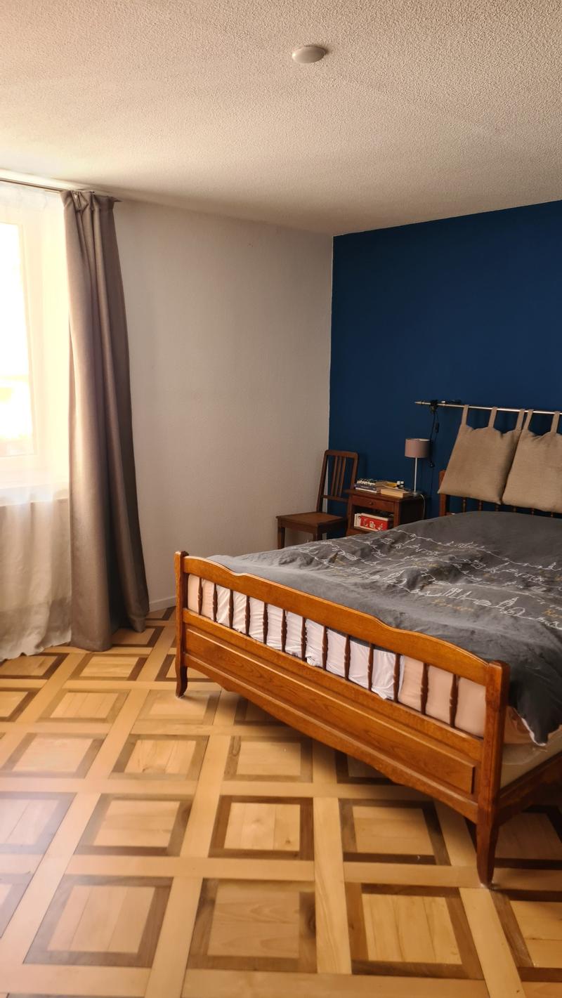 bedroom with wooden bed, blue wall, white wall, wooden chair, nightstand, lamp, window with curtain